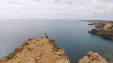 Deniz kenarında bir kayaya oturan genç kadın