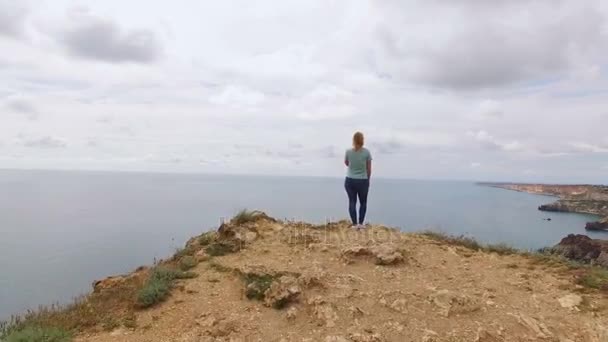 Молода жінка залишається на скелі біля моря — стокове відео