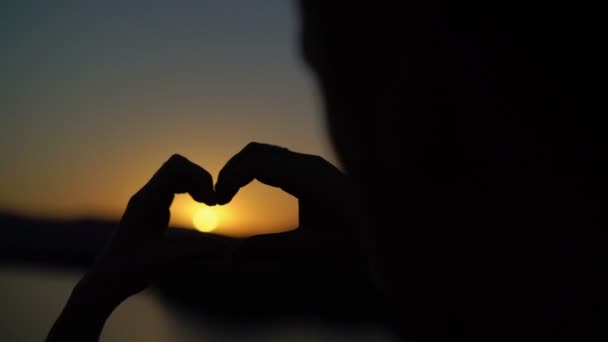 Pareja joven hace el corazón de las manos en la puesta del sol — Vídeos de Stock
