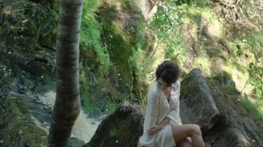 Şelale yakınındaki bir kayaya oturan genç kadın