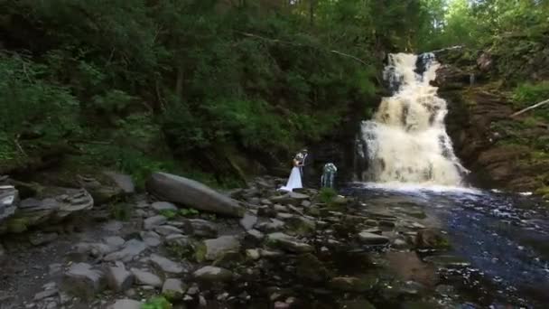 滝の近くを歩く若い結婚式のカップル — ストック動画