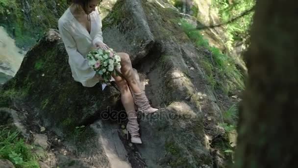 Şelale yakınındaki bir kayaya oturan genç kadın — Stok video