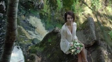 Şelale yakınındaki bir kayaya oturan genç kadın