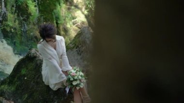 Şelale yakınındaki bir kayaya oturan genç kadın