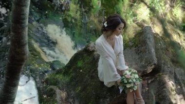 Şelale yakınındaki bir kayaya oturan genç kadın