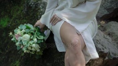 Şelale yakınındaki bir kayaya oturan genç kadın