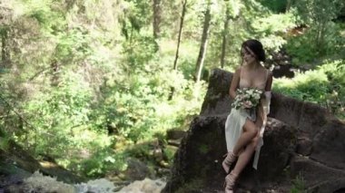 Şelale yakınındaki bir kayaya oturan genç kadın