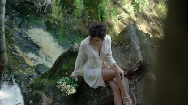 Wanita muda duduk di batu dekat air terjun — Stok Video