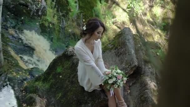 Молода жінка сидить на скелі біля водоспаду — стокове відео