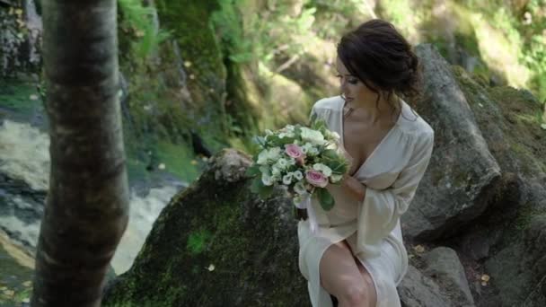 Młoda kobieta siedzi na skale, niedaleko wodospadu — Wideo stockowe