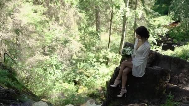 Jovem mulher sentada em uma rocha perto da cachoeira — Vídeo de Stock