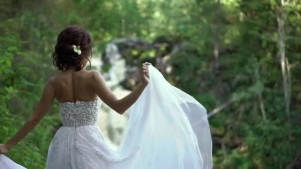 Mariée encerclant et agitant robe près de cascade — Video