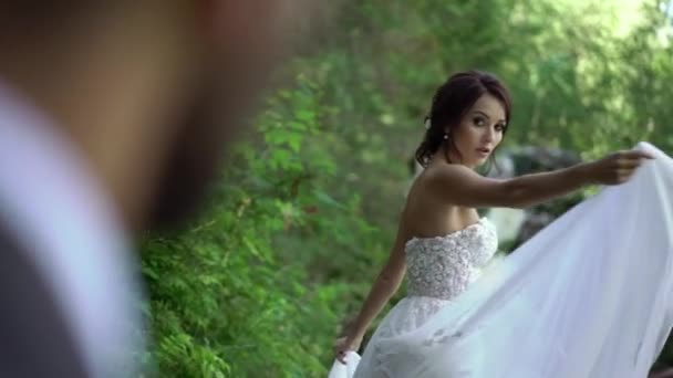 Bruden cirklande och viftande klänning nära waterfall — Stockvideo