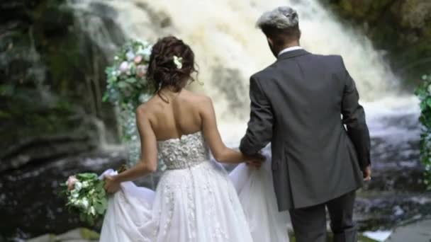 Jeune couple de mariage marchant à la cérémonie près de cascade — Video