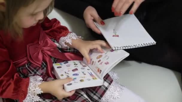 Mother and small daughter watching books with stickers — Stock Video