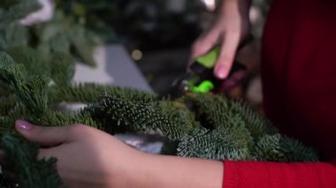 Noel ve yeni yıl kutlaması için hazırlık. Kız ladin dallarından bir çelenk yapıyor. Tatil için dekorasyon atölyesi