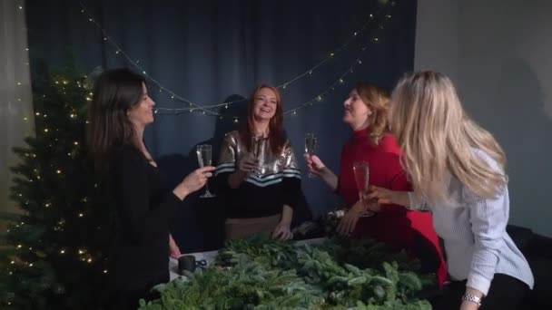 Preparazione per la celebrazione del Natale e del nuovo anno. Festa festiva, giovani donne battono i bicchieri con champagne, divertimento. Le ragazze fanno una ghirlanda di rami di abete. Workshop sul design per le vacanze — Video Stock