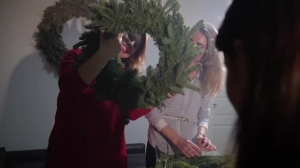 크리스마스와 새해를 기념하기 위한 준비. 소녀들은 가문비나무 가지로 화환을 만듭니다. 축일 장식을 하는 작업장. — 비디오