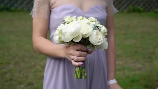 Giovane sposa in abito da sposa che tiene fiori bouquet in un parco. Bianco moda abito di lusso — Video Stock