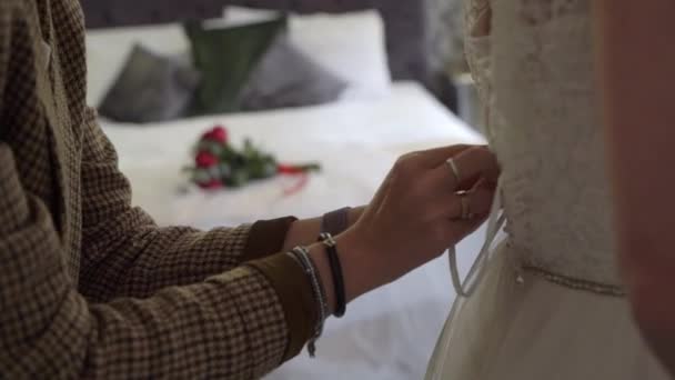 Koszorúslány segít a fiatal menyasszonynak felvenni az esküvői ruháját. Luxus menyasszonyi ruha — Stock videók