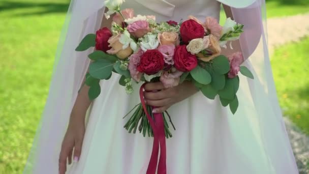 Young bride in wedding dress holding bouquet flowers in a park. White luxury gown fashion — Stock Video