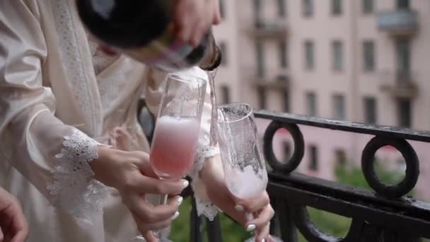 Jong stel opent fles champagne en giet glazen in op het balkon. Alcoholische dranken en dranken. — Stockvideo