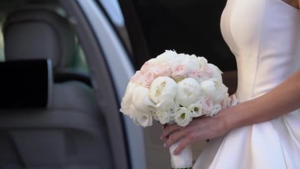 Młoda panna młoda w sukni ślubnej trzymająca kwiaty bukietu w mieście. Biały luksusowy strój mody — Wideo stockowe