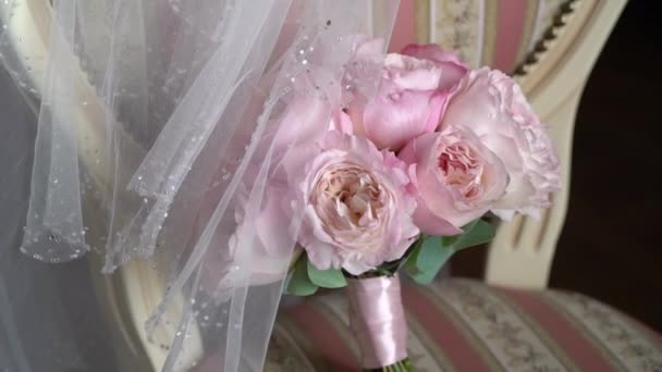 Kytice z růžových růží. Svatební kytice nevěsty. Ranní přípravy novomanželů. Květinové aranžmá na židli v ložnici - květiny a závoj. — Stock video