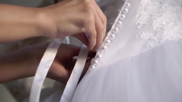新婦付添人は若い花嫁が彼女の結婚式の服を着るのを助ける。ラグジュアリーブライダルガウン — ストック動画