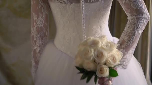 Jonge bruid in trouwjurk met boeket bloemen binnen. Witte luxe jurk mode — Stockvideo
