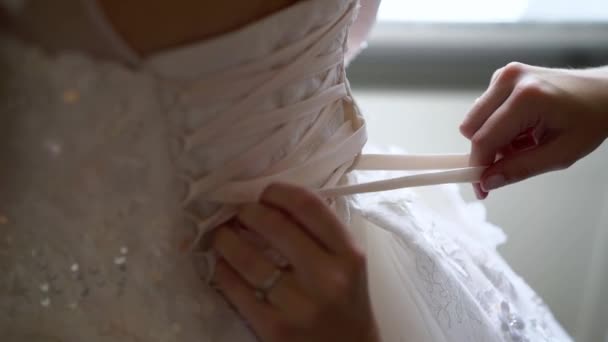 Подружка невесты помогает молодой невесте надеть свадебное платье. Роскошное свадебное платье — стоковое видео