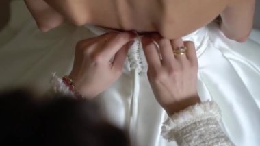 Nedime, genç gelinin gelinliğini giymesine yardım ediyor. Lüks gelinlik.