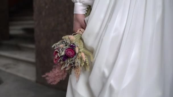 Fiatal menyasszony menyasszonyi ruhában csokorvirággal a kezében egy városban. Fehér luxus ruha divat — Stock videók