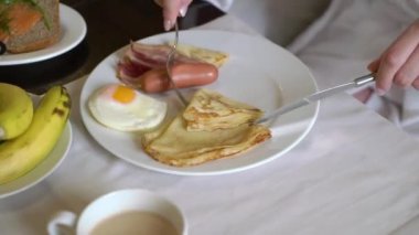 Sabahları kahvaltı yapan bir kadın. Tavada yumurta, krep ve sosis..