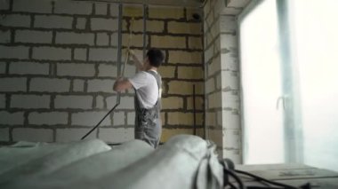 İnşaat alanında çalışan bir işçi, duvarlarla sarı fünyeyi karıştırıyor. Daire ya da evin yenilenmesi ve onarımı