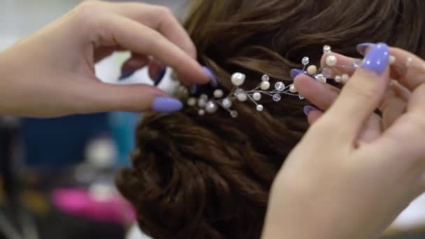 Ювелірні вироби в волоссі, прикрашають зачіску для жінки. Перукарня, що працює з брюнеткою нареченої на весіллі — стокове відео