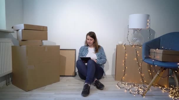 Жінка рухається в новому будинку. Сидячи на підлозі і розслабляючись з планшетом — стокове відео