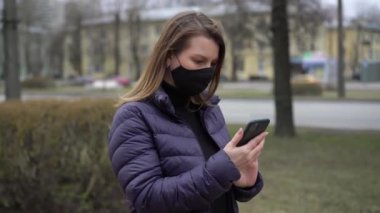 Cep telefonu olan bir şehirde koruyucu maskeli bir kadın. covid-19 koronavirüs