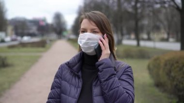 Cep telefonu olan bir şehirde koruyucu maskeli bir kadın. covid-19 koronavirüs