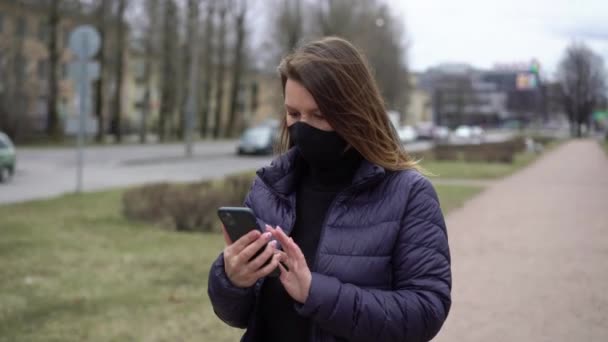 Mulher no rosto máscara protetora em uma cidade com telefone celular. covid-19 coronavírus — Vídeo de Stock