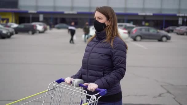 Женщина в защитной маске в тележке супермаркета на коронавирусе ковид-19 — стоковое видео