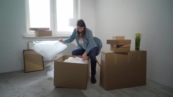 Mudándose a un nuevo hogar. Mujer abriendo una caja de cartón, dueño del apartamento — Vídeo de stock