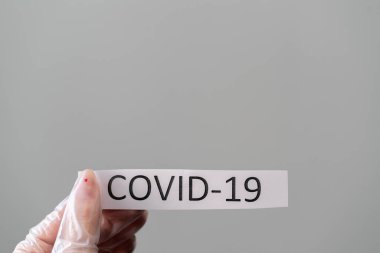 Koruyucu lateks eldivenli kadın elinde kovid 19 koronavirüs metni olan bir kağıt tutuyor.
