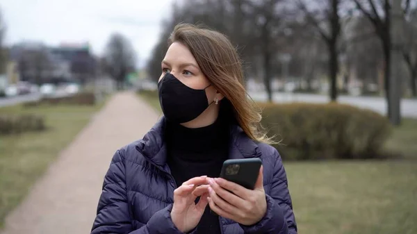 Cep telefonu olan bir şehirde koruyucu maskeli bir kadın. covid-19 koronavirüs