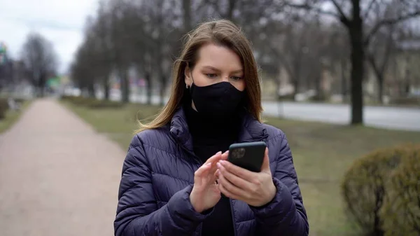 Cep telefonu olan bir şehirde koruyucu maskeli bir kadın. covid-19 koronavirüs