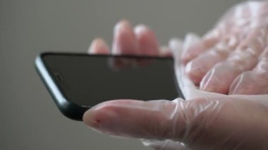 Koruyucu eldivenli bir kadın cep telefonunu ıslak bezle temizliyor, dezenfekte ediyor.