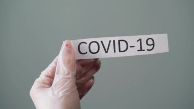 Koruyucu lateks eldivenli kadın elinde kovid 19 koronavirüs metni olan bir kağıt tutuyor.
