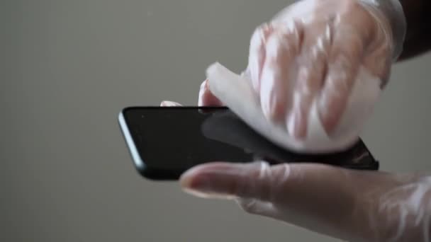Vrouw in beschermende handschoenen schoonmaken van mobiele telefoon met natte doek, desinfecteren — Stockvideo