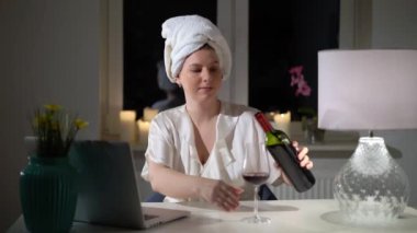 Bilgisayarın başında çalışan genç bir kadın akşamları ev ofisinde şarapla birlikte çalışıyor.
