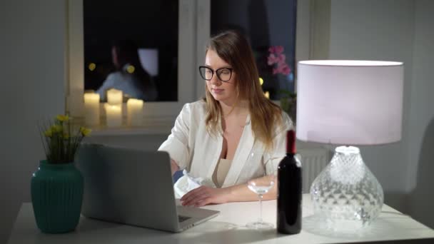 Mujer joven que trabaja en el ordenador portátil en la oficina en casa por la noche con vino — Vídeo de stock